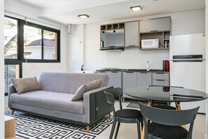Ein kompakter Wohnbereich mit Sofa, Stühlen, Esstisch, Mikrowelle und Kühlschrank.