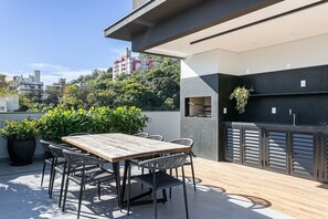 Una terraza en la azotea con mesa y sillas de madera, plantas en macetas y una cocina de exterior moderna.