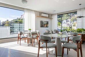 Ein moderner Essbereich mit großem Tisch und Stühlen, großen Fenstern mit Vorhängen und Blick auf Gebäude und Grünflächen.