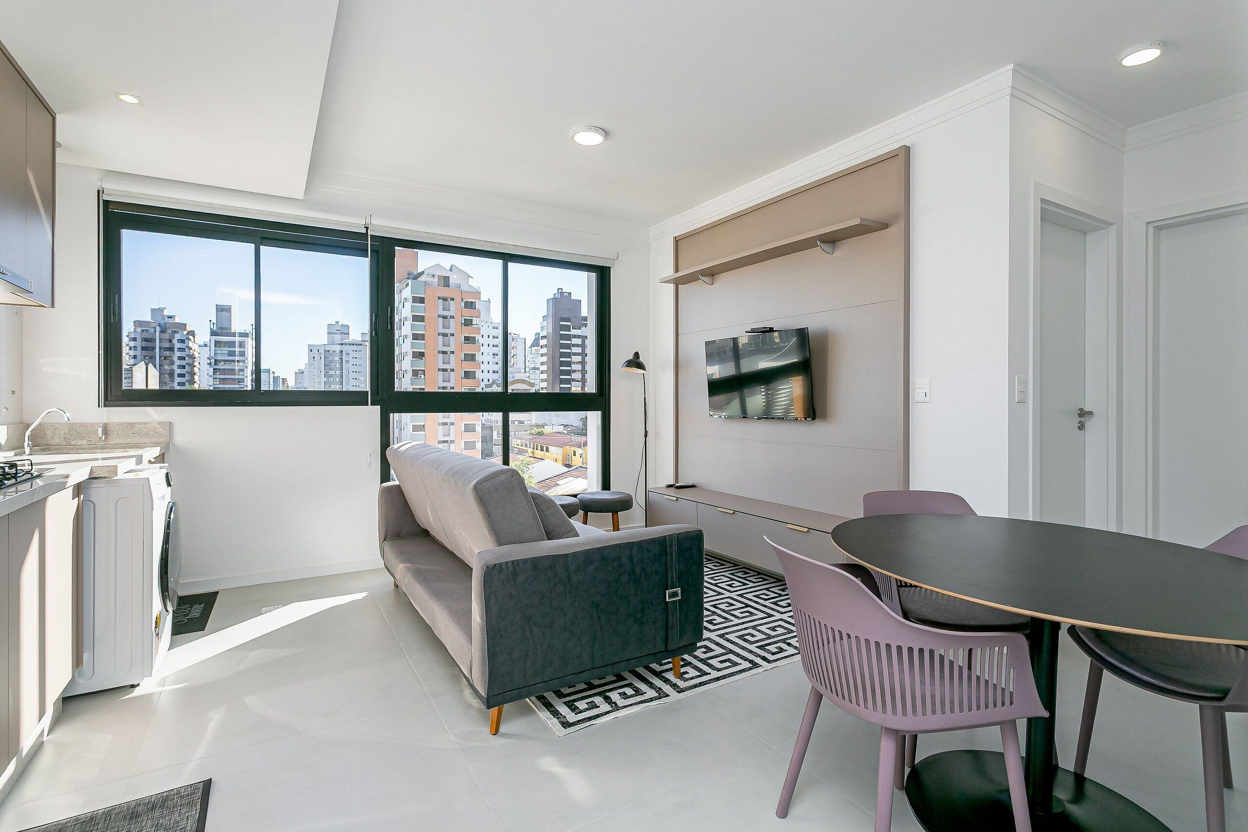A modern apartment with a sofa, dining table, chairs, a washing machine, and a TV.