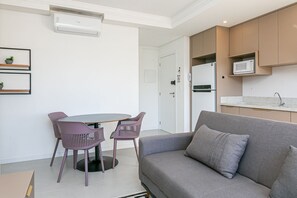 Ein modernes Wohnzimmer mit einem grauen Sofa, violetten Sesseln, einem kleinen Tisch und einer Küchenzeile mit einer Mikrowelle.