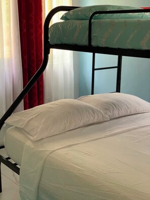 Ein Etagenbett mit einer Matratze und Kissen, ein Fenster mit Vorhängen und einem Metallgestell.