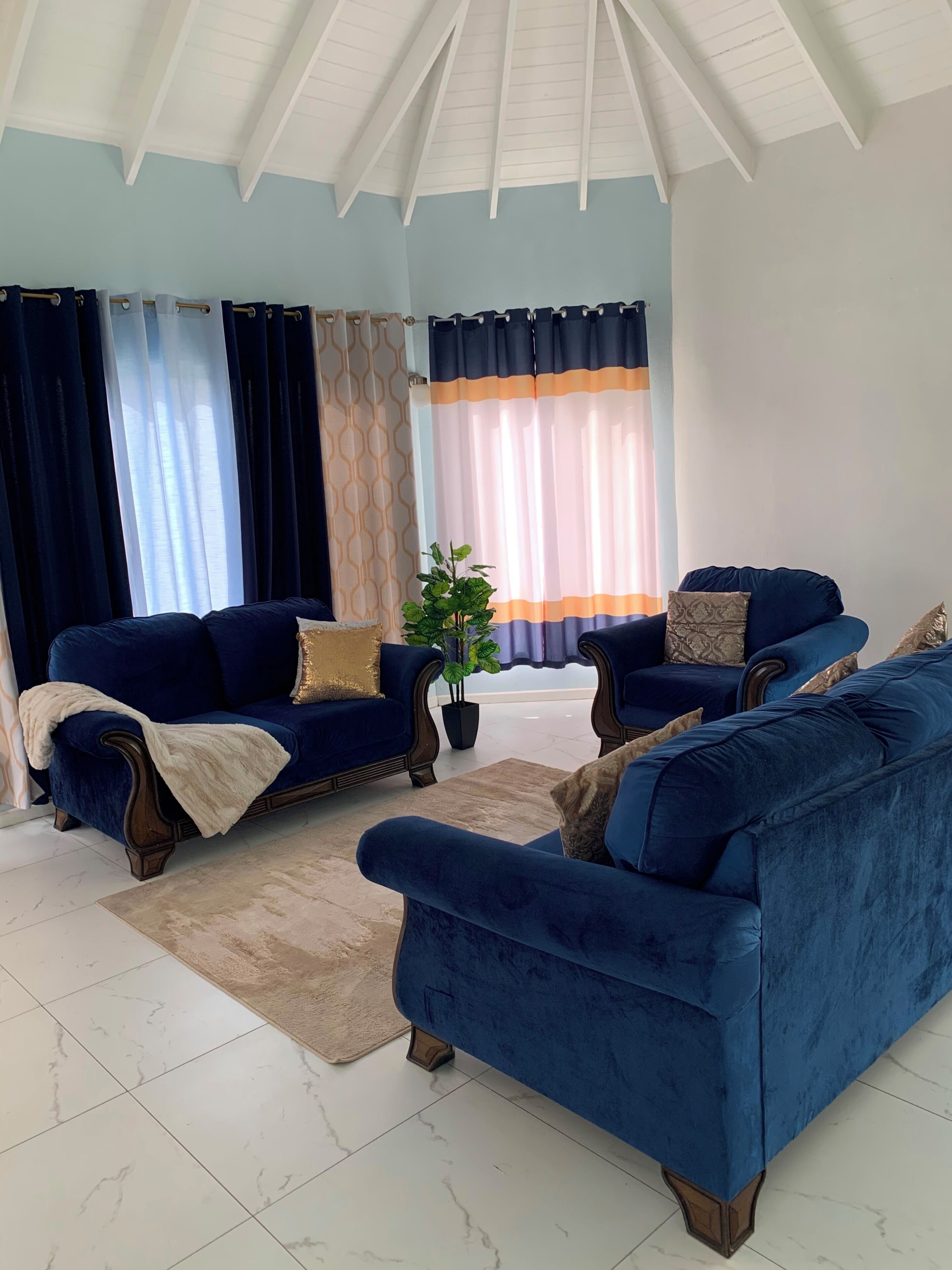 A living room with a high ceiling, two blue sofas, a coffee table, and a potted plant.