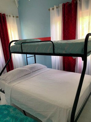 A bunk bed with a green mattress and white bedding in a room with blue walls and red curtains. - Tremendous 3-bedroom house with AC in Anse La Raye (Anse La Raye)