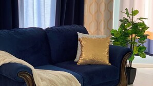 Un canapé bleu foncé agrémenté d’un coussin doré, d’un plaid blanc et d’une plante en pot.