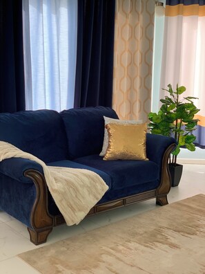 Ein dunkelblaues Sofa mit einem goldfarbenen Zierkissen, einer weißen Decke und einer Topfpflanze.