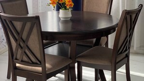 Une table à manger avec six chaises, un vase rempli de fleurs et, au fond, un rideau bleu.