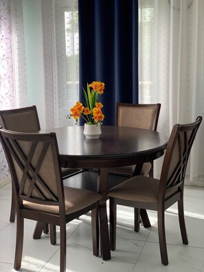 Ein Esstisch mit sechs Stühlen, eine Vase mit Blumen und ein blauer Vorhang im Hintergrund.