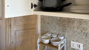 Una cocina con un armario blanco, un colgador para ollas y una estantería con platos apilados.