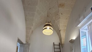 Un dormitorio con un techo alto y abovedado, una cama, un aparador, una escalera y una ventana.