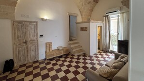 Una habitación con suelo a cuadros, un sofá, un armario de madera, una puerta y una escalera que sube a otra habitación.