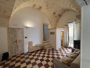 Ein Zimmer mit Schachbrettmuster-Bodenbelag, einer Couch, einem Holzschrank, einer Tür und einer Treppe, die in ein weiteres Zimmer führt.