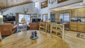 A spacious living area with a wooden ceiling, a fireplace, a dining table with bear figurines, and a kitchen with wooden cabinets and a stainless steel refrigerator. - Woodland Truckee Retreat (Truckee)