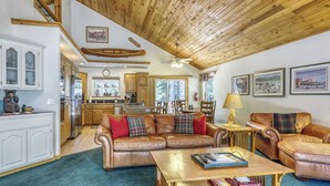 A spacious living room with a wooden ceiling, a large brown leather sofa, a coffee table, and a view of the kitchen in the background. - Woodland Truckee Retreat (Truckee)
