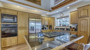 A kitchen with wooden cabinets, stainless steel appliances, a glass island, and a window with a view. - Woodland Truckee Retreat (Truckee)