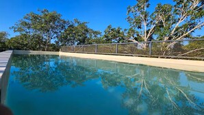 A swimming pool with a clear blue water surface, surrounded by trees and a fence. - Cuatro Elementos By Gestores Studio (Tulum)