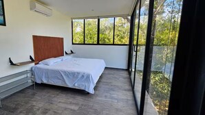 A bedroom with a bed, a bench, a painting, and a balcony with a view. - Cuatro Elementos By Gestores Studio (Tulum)