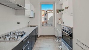 A narrow kitchen with a gas stove, oven, and a window with a view of buildings. - Graffiti House Luxury Apartment (La Spezia)
