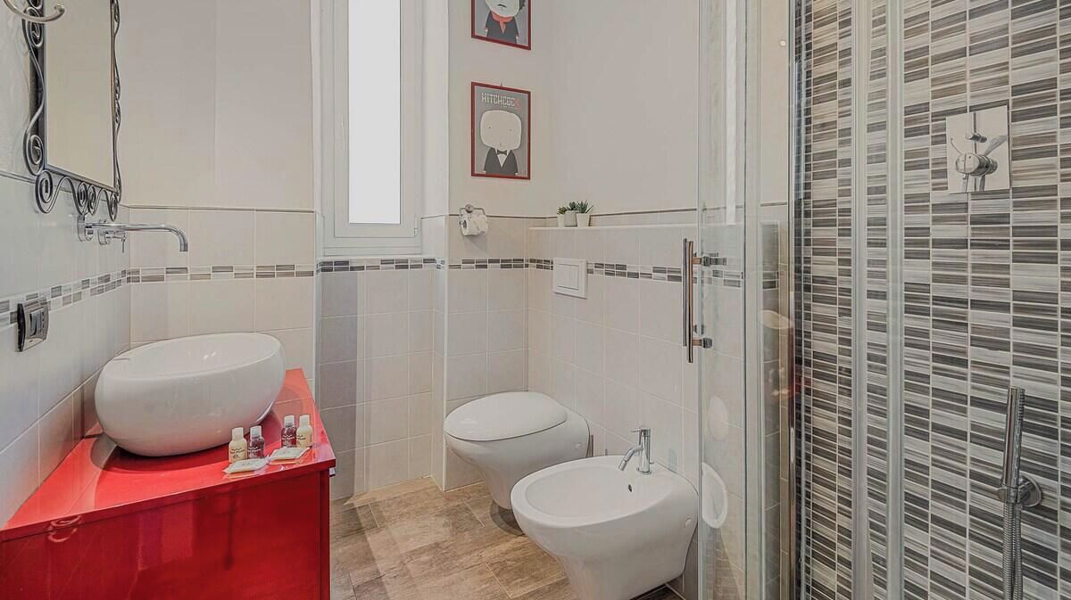 A bathroom with a red vanity, two sinks, a toilet, and a shower area.
