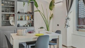 A dining area with a white table, chairs, and a bookshelf with books and decorative items. - Graffiti House Luxury Apartment (La Spezia)