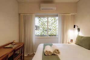 A hotel room with a bed, a desk, a window with curtains, and an air conditioner. - Hestia en Arenales 2900 (Buenos Aires)