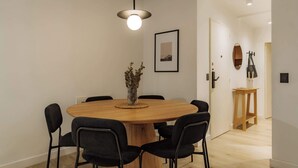 A dining area with a round wooden table, black chairs, a hanging light fixture, a framed picture on the wall, and a door with a mirror and coat rack. - Hestia en Arenales 2900 (Buenos Aires)