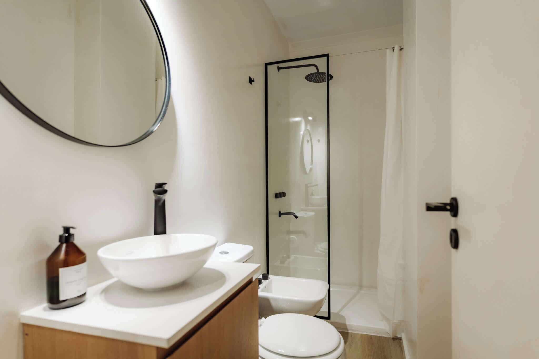 Een badkamer met een witte wastafel, een grote spiegel, een douche met glazen wanden en een toilet.