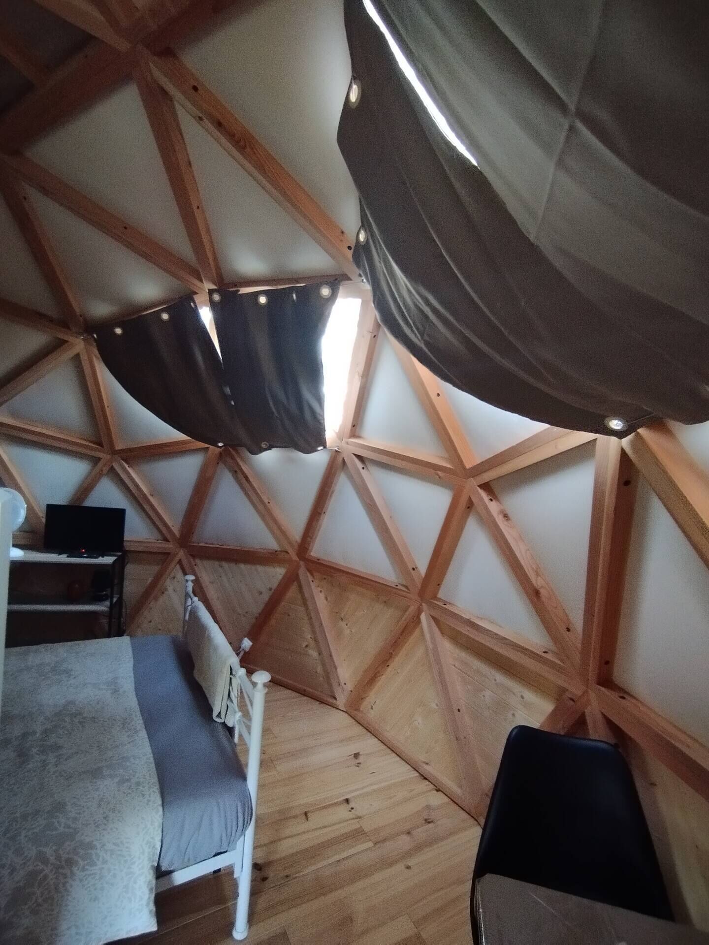 A room with a wooden ceiling structure, a bed, a chair, and a television.