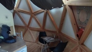 A compact room with a wooden floor, a small table with chairs, a white refrigerator, and a window with black curtains.