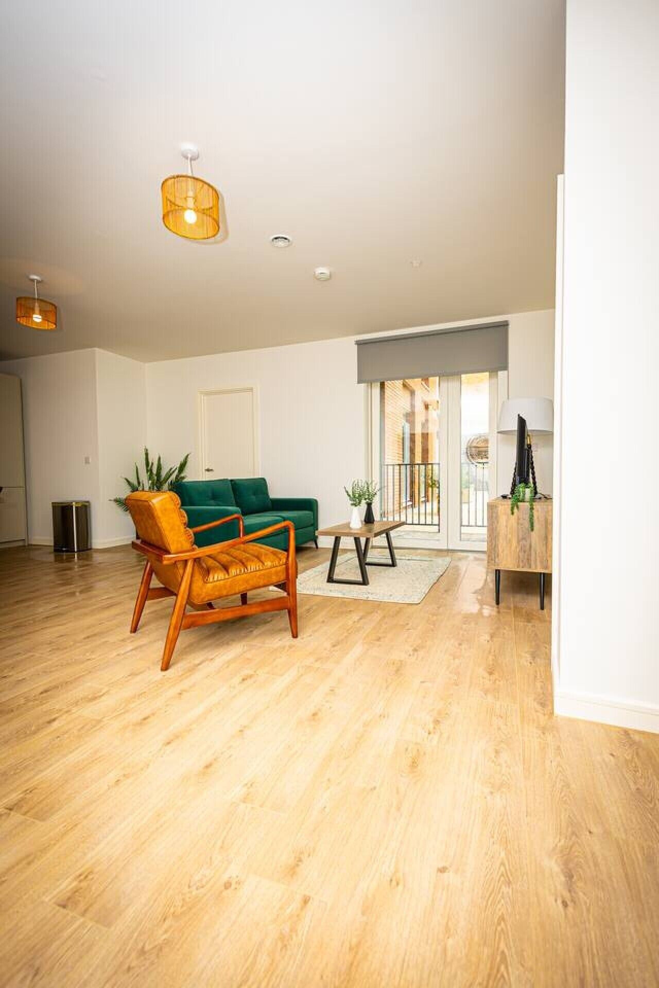 Un salón espacioso con piso de madera, un sofá verde, un sillón de madera, una mesita y una lámpara.