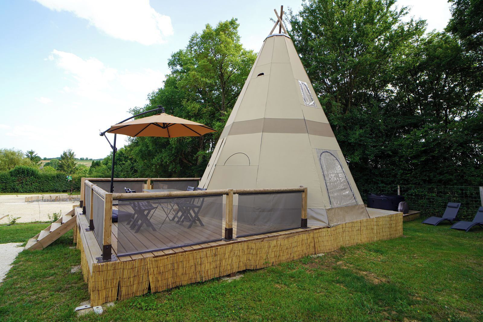 A teepee-style tent with a wooden deck and outdoor seating.