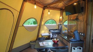 Une pièce triangulaire de taille modeste, comprenant une table à manger, des chaises, une machine à café et un téléviseur fixé au mur.