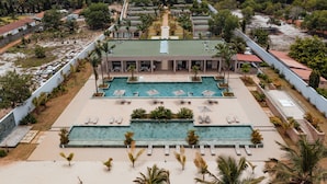 A resort with multiple swimming pools, lounge areas, and a central building with a green roof. - Escapade Hotel (Assinie)