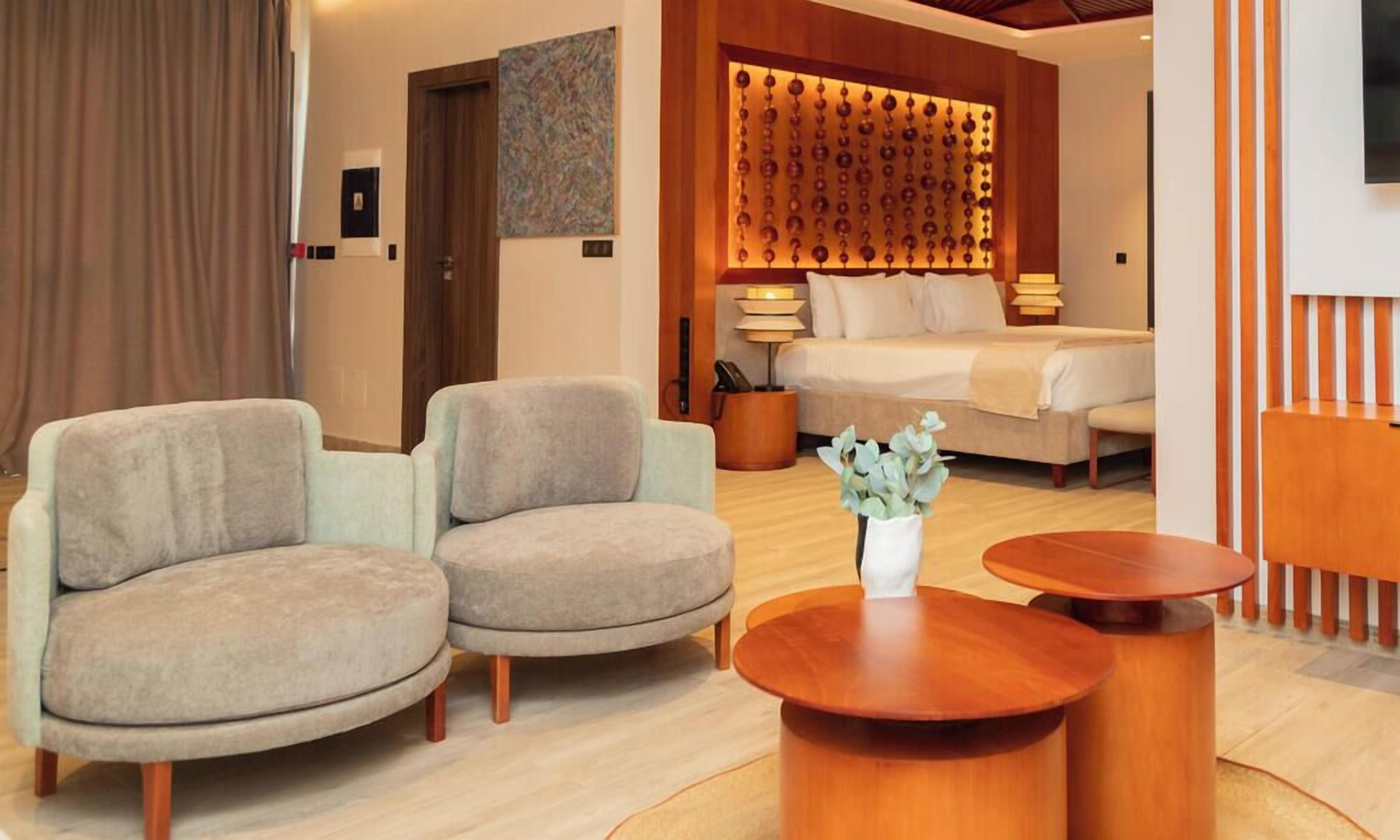 Een hotelkamer met een bed, twee fauteuils, een bijzettafeltje en een decoratief wandpaneel.