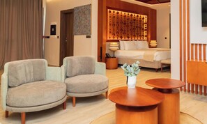 Quarto de hotel com uma cama, duas poltronas, uma mesa de centro e um painel decorativo na parede.
