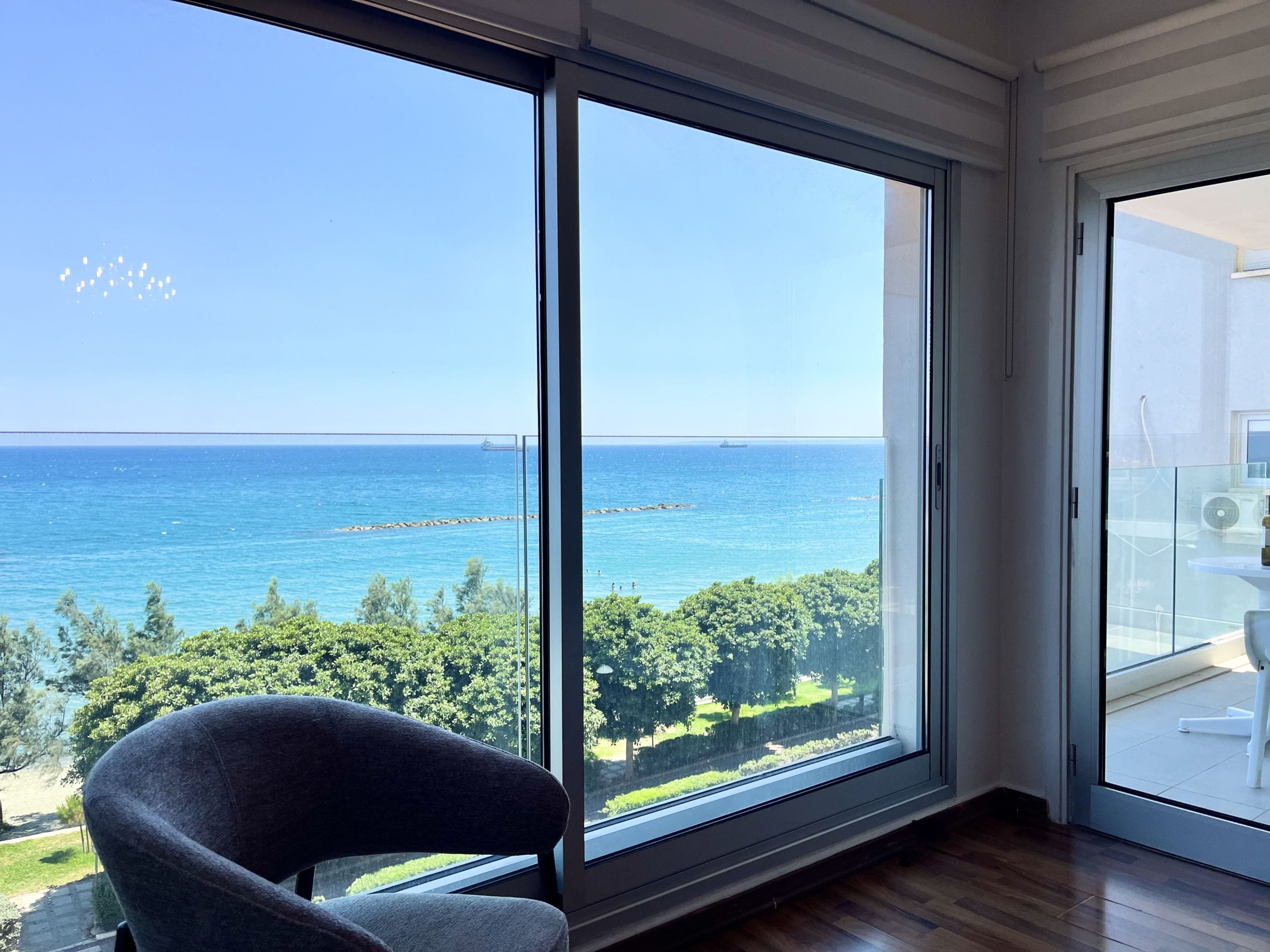 A room with a large window offering a view of the sea and greenery.