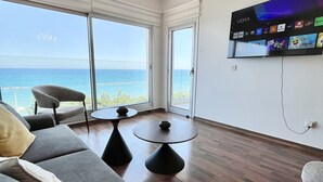 A modern living room with a large TV, a sofa, a chair, and a dining table. - 159 LIM - Stay Sea Pearl Apartment (Limassol)