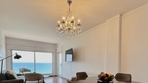 A spacious living area with a dining table, chairs, a chandelier, a sofa, a TV, and a view of the sea. - 159 LIM - Stay Sea Pearl Apartment (Limassol)