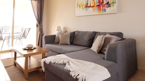 En stue med sofa, sofabord, lampe, et maleri og udsigt gennem et vindue.