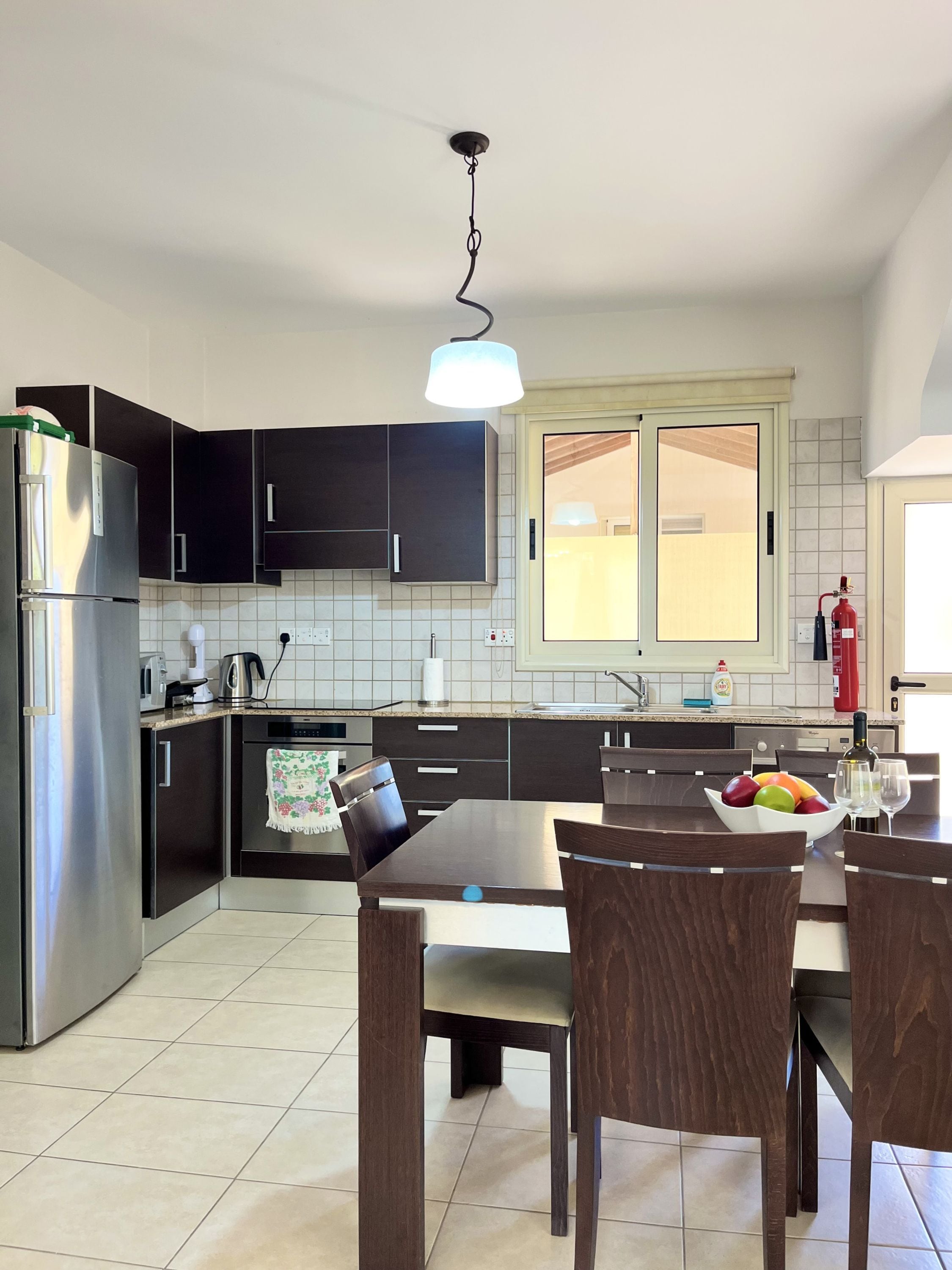 Una cocina moderna con armarios oscuros, un refrigerador de acero inoxidable, una mesa con sillas y un frutero.