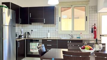 Una cocina moderna con armarios oscuros, un refrigerador de acero inoxidable, una mesa con sillas y un frutero.