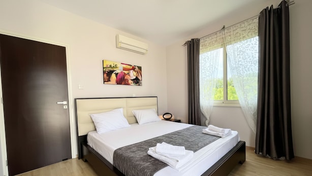 Habitación de hotel con una cama, un cuadro en la pared, aire acondicionado, una ventana con cortinas y una puerta.