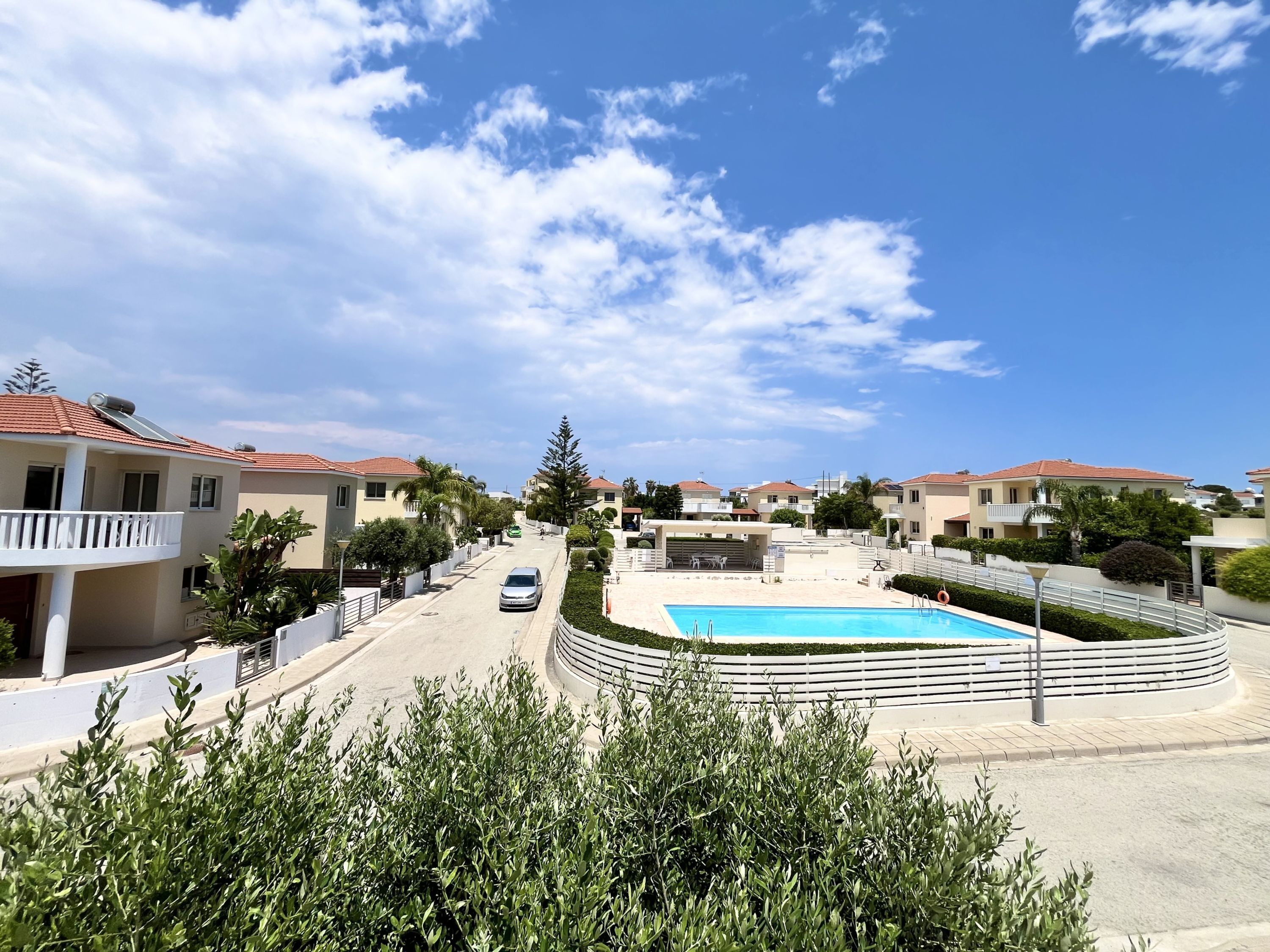 Zona residencial con piscina, casas con techos de tejas rojas y cielo despejado.
