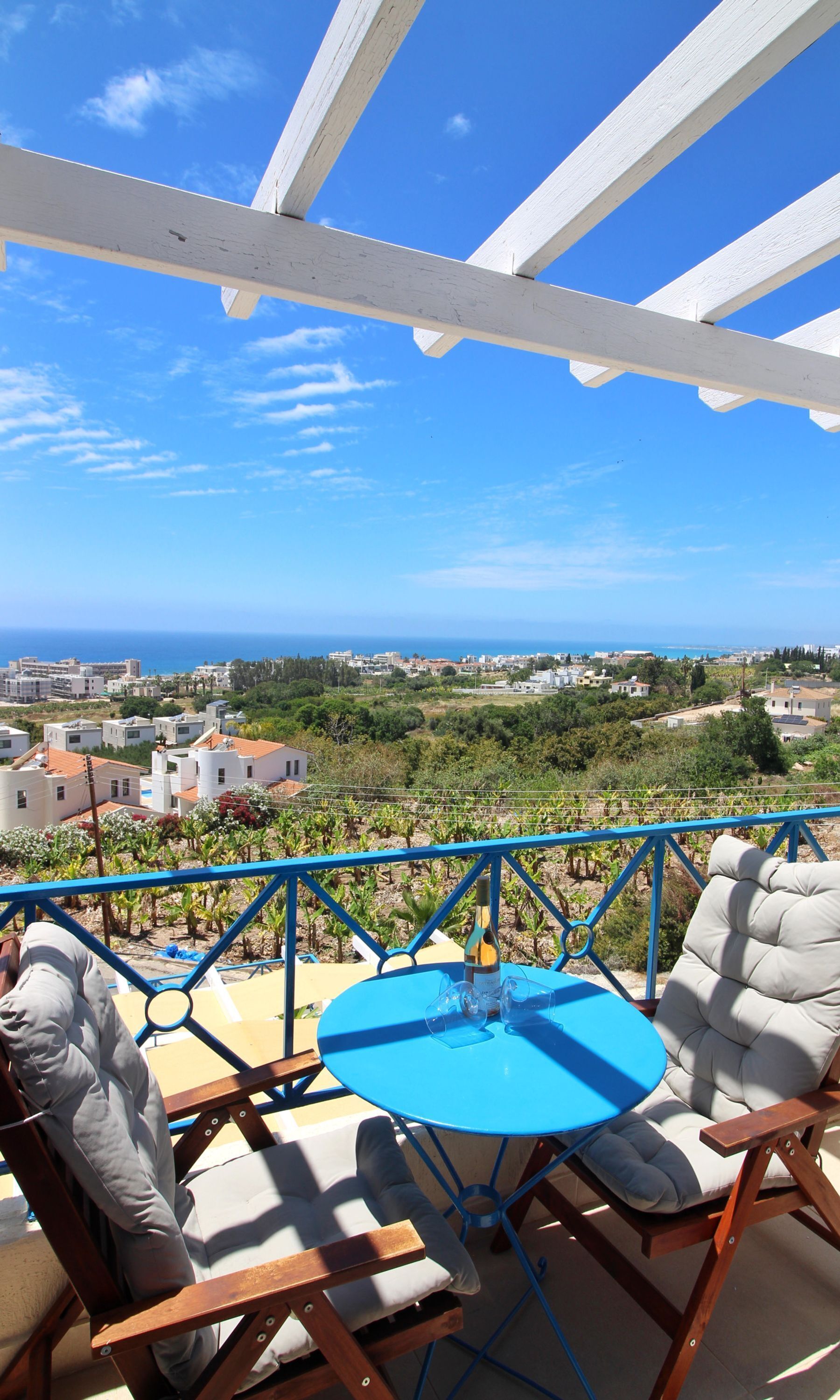 Un balcon avec une table et des chaises, donnant sur une ville côtière et des vignobles.
