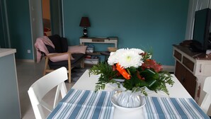 Zona de dinar amb taula ben posada per a dues persones, una cadira, un vas amb flors, una làmpada i un petit armari.