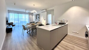 Una cocina moderna con una isla central, un comedor con mesa y sillas, y una sala de estar con sofá y televisor.