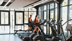 Un gimnasio con cintas de correr, una banca y ventanas amplias.