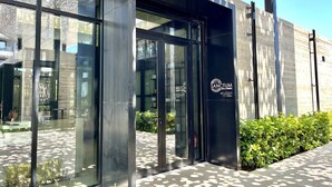 Fachada moderna de un edificio con puertas de vidrio, un logotipo y un camino que lleva a la entrada.