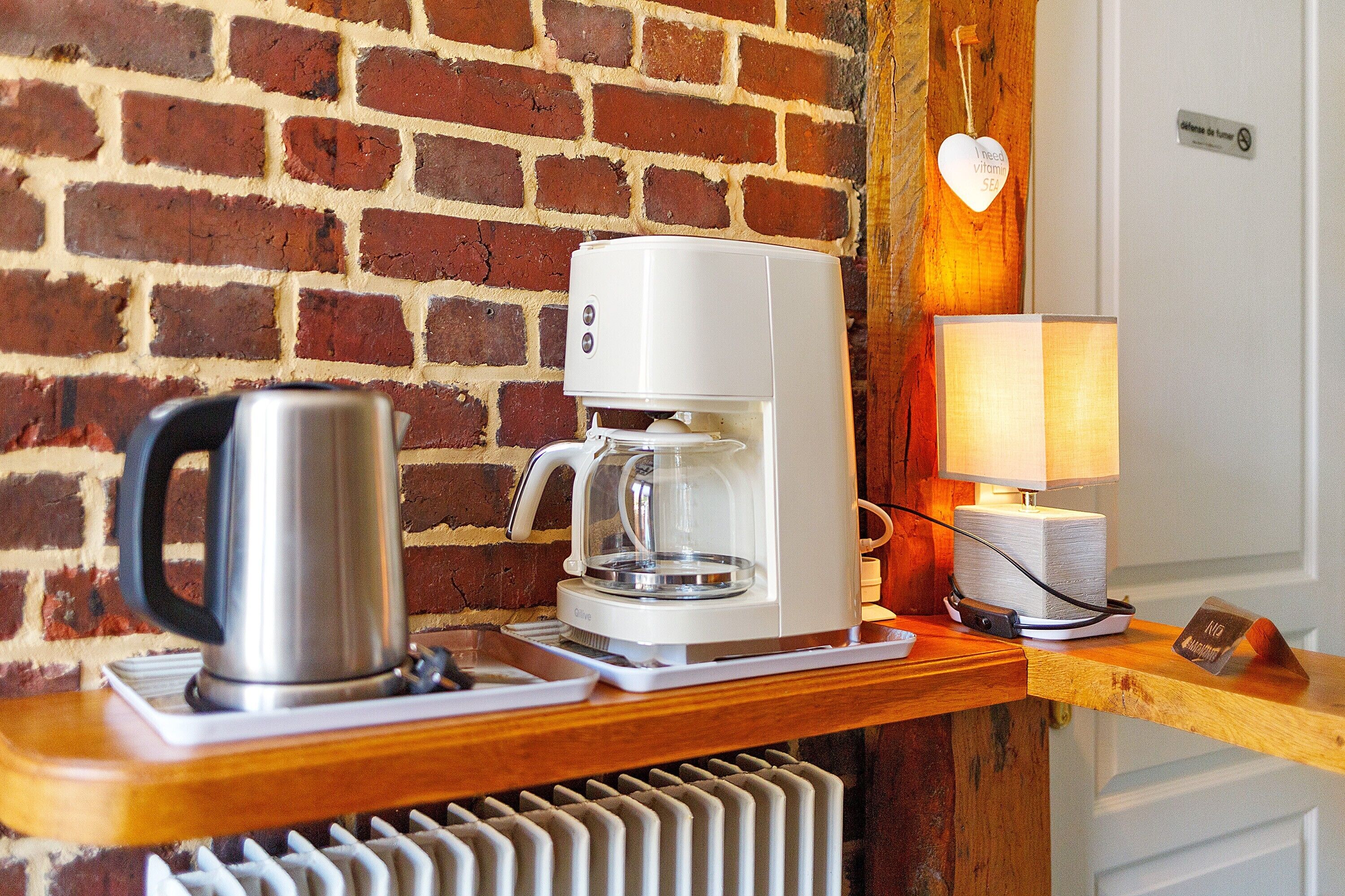 A coffee maker and kettle on a wooden counter with a brick wall background.
