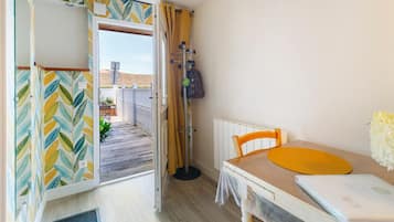 Um quarto pequeno com uma mesa de madeira, uma cadeira, um radiador e vista para uma varanda com plantas.